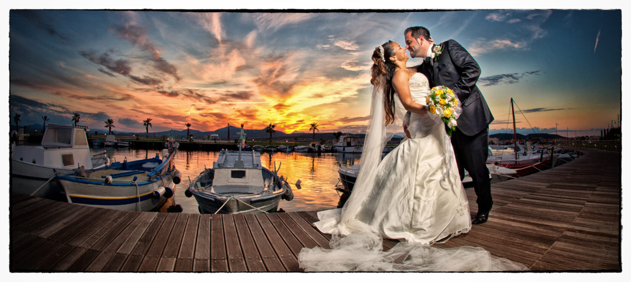 Sposi in passerella con barche attraccate al molo. Foto scattata da Giuseppe Ortu fotografo fine art specializzato in matrimoni a Olbia.