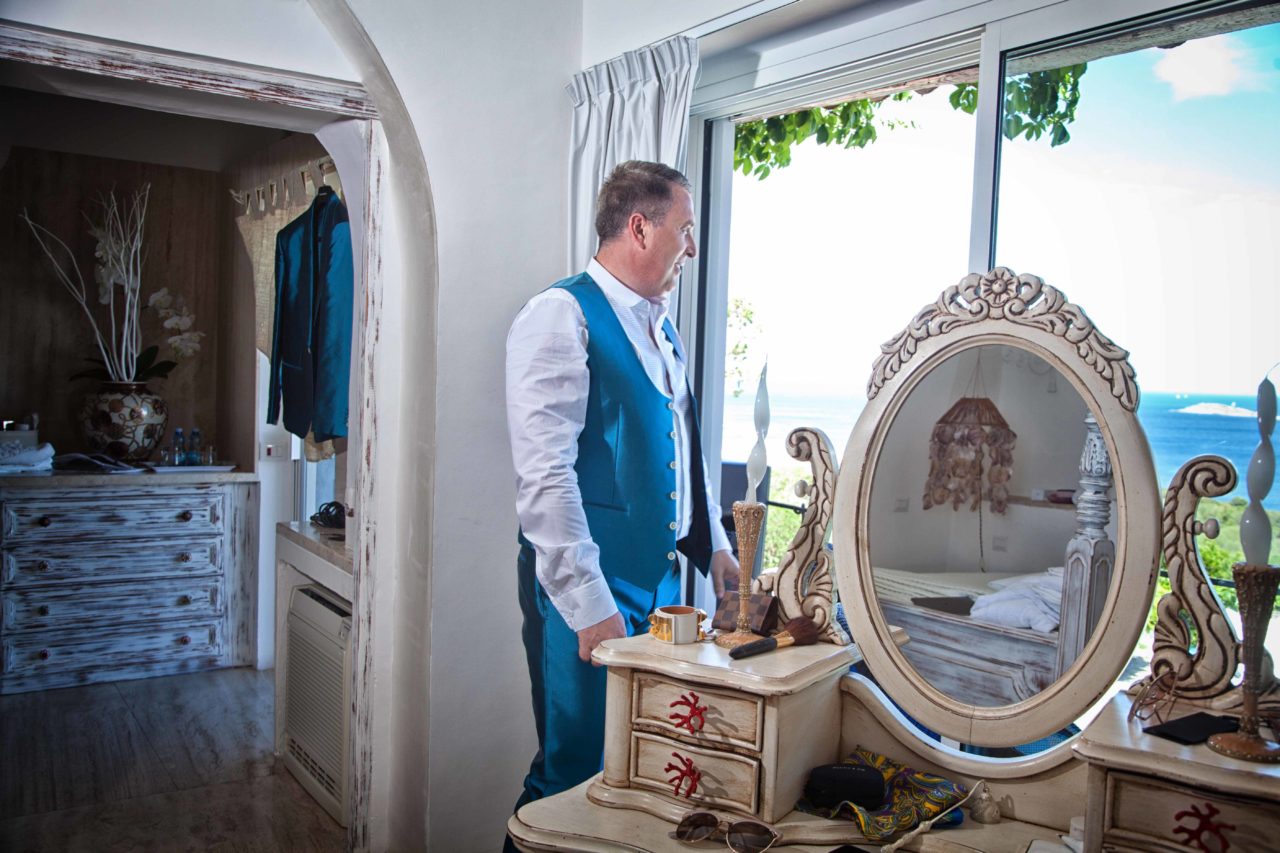 Sposo che guarda il mare dalla finestra. Foto scattata da Giuseppe Ortu fotografo specializzato in matrimoni a Olbia.