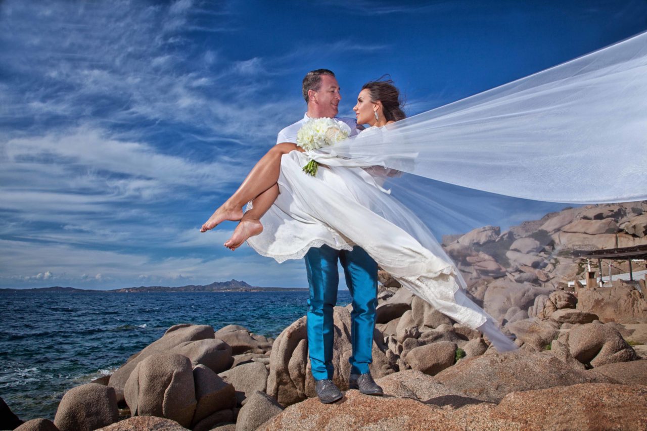 Sposa in braccia allo sposo sugli scogli in riva al mare. Foto scattata da Giuseppe Ortu fotografo specializzato in matrimoni a Olbia.