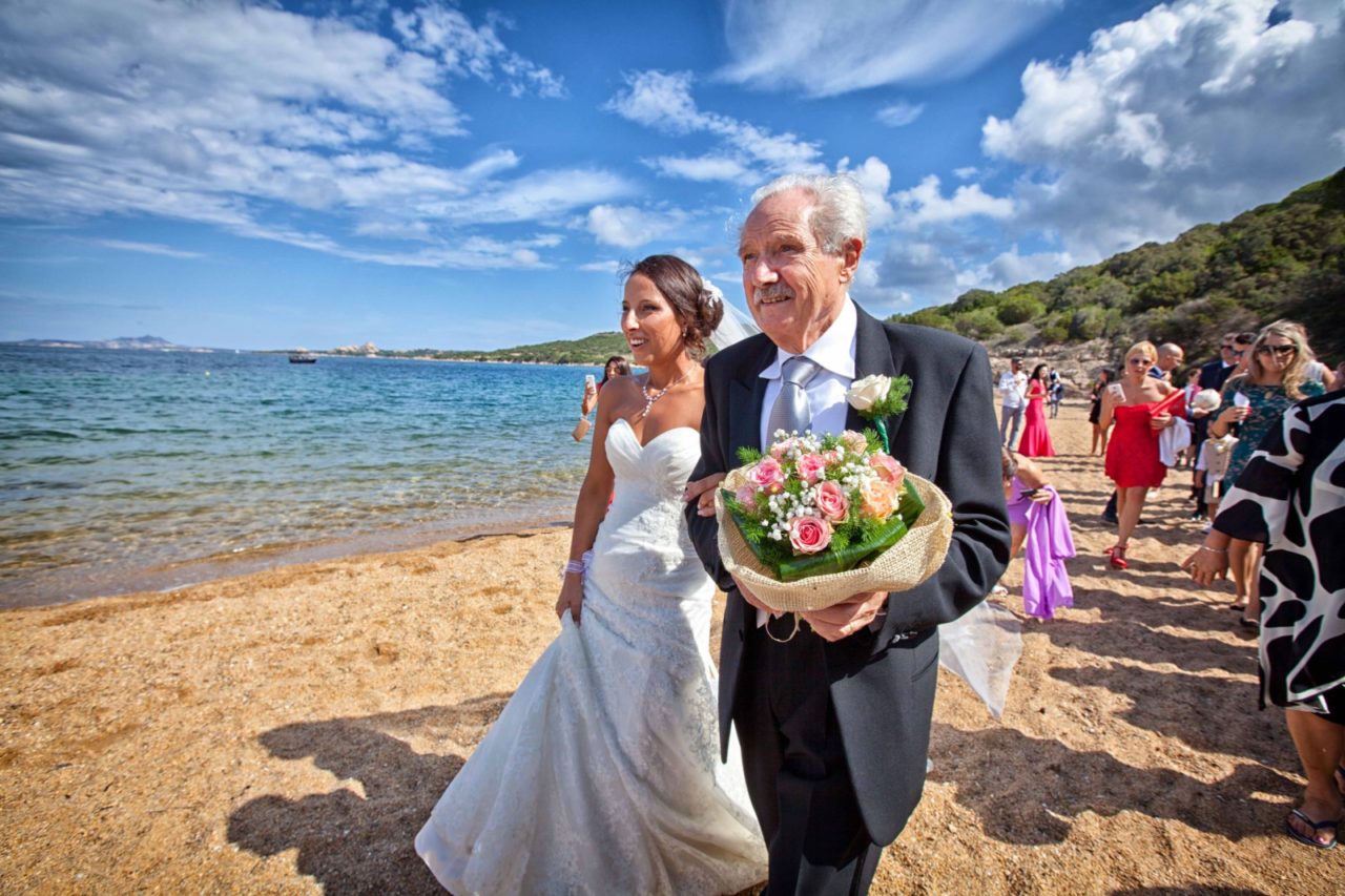 Sposa accompagnata sulla spiaggia. Fotografia scattata da Giuseppe Ortu fotografo specializzato in matrimoni a Olbia.